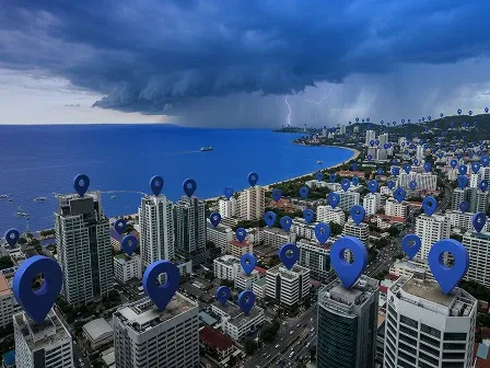 Business intelligence for reinsurance hero image showing a coastal city with location pins on buildings and an approaching storm offshore.