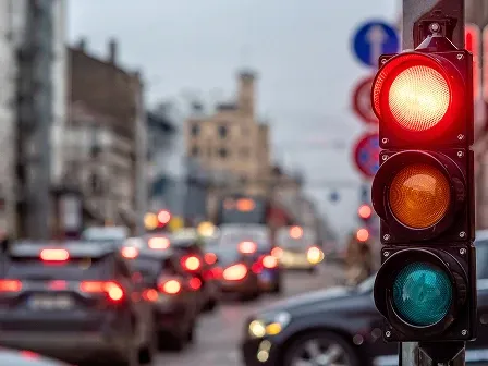 Close-up of a red traffic light with blurred city traffic and car headlights in the background