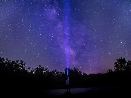 Guy shining flashlight into the sky.